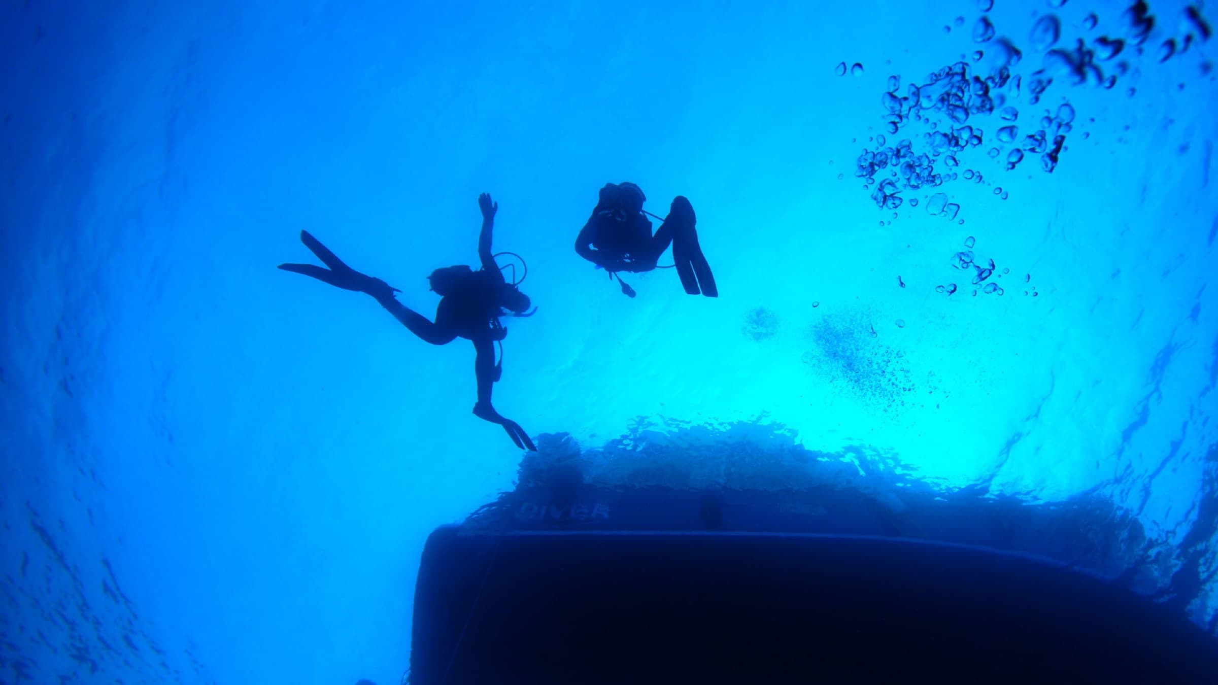 Two divers working beneath a boat hull below the waterline.